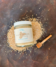 Load image into Gallery viewer, Jar of oatmeal milk and honey sugar body scrub on a dark surface with a honey dipper.